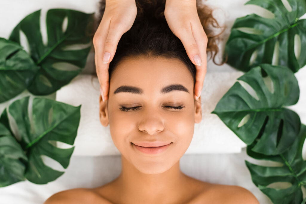 Relaxed woman receiving head massage among green leaves